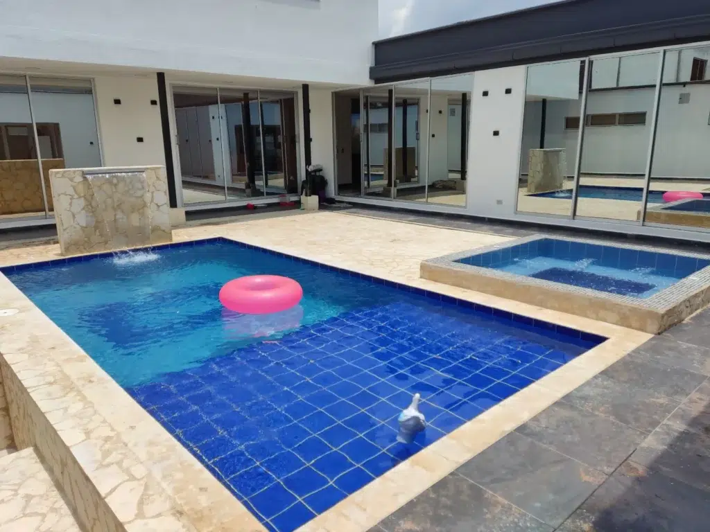 Piscina moderna creada por Piscinas Bluespace en Belén, Medellín, con azulejos azules, cascada decorativa y jacuzzi integrado. Diseño residencial que combina lujo y comodidad en un espacio exclusivo y contemporáneo