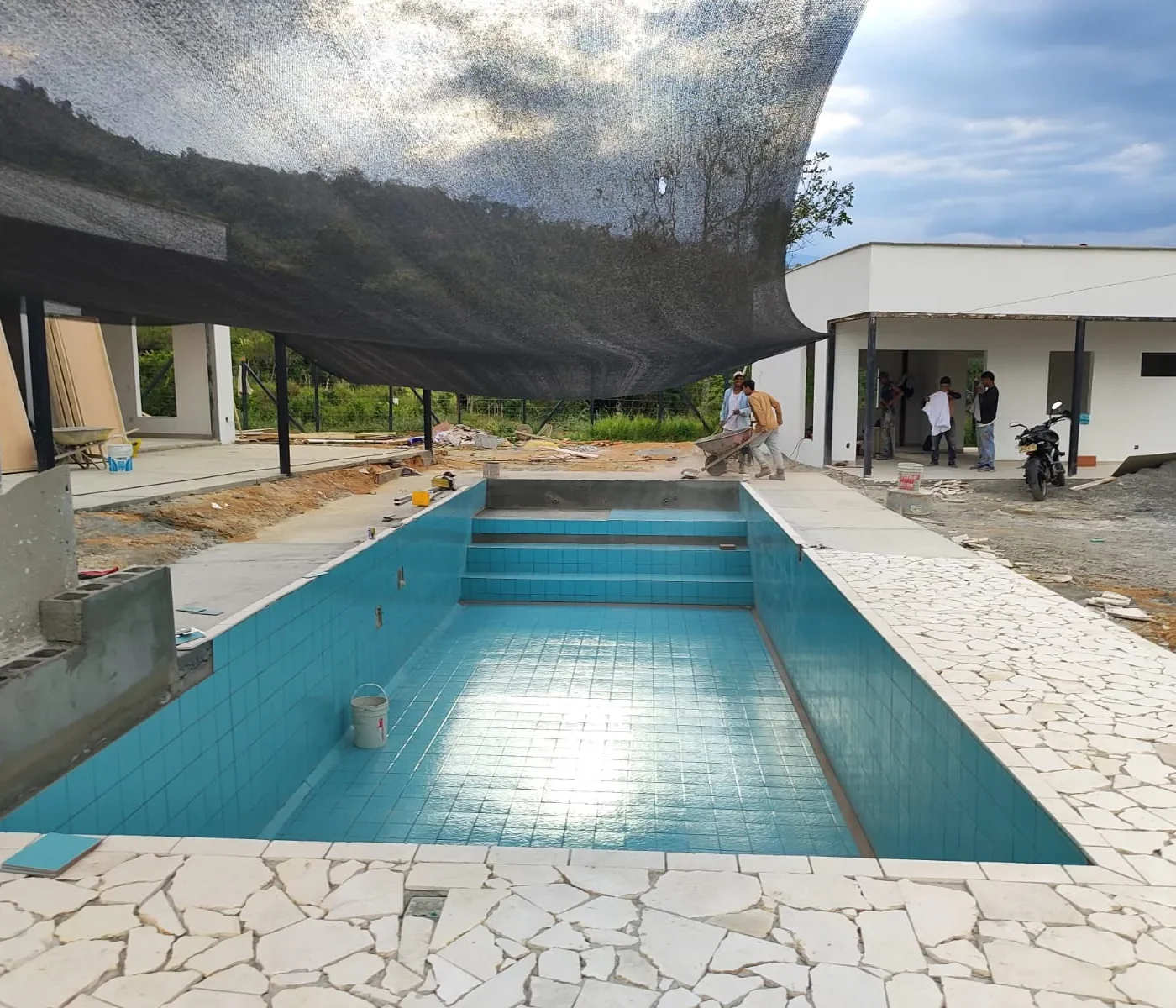 Piscina en construcción por Piscinas Bluespace en Valparaíso, con revestimiento de azulejos azules y borde de piedra blanca, diseñada para ofrecer durabilidad y estética. Proyecto personalizado de piscina, resaltando la calidad de los materiales y el enfoque en detalles durante la instalación.