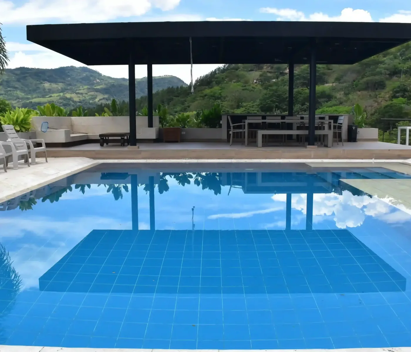 Piscina moderna construida por Piscinas Bluespace en Asiria, con revestimiento de azulejos azules y un entorno natural montañoso. Espacio de recreación diseñado con áreas de descanso y sombra, ofreciendo un ambiente de lujo y tranquilidad