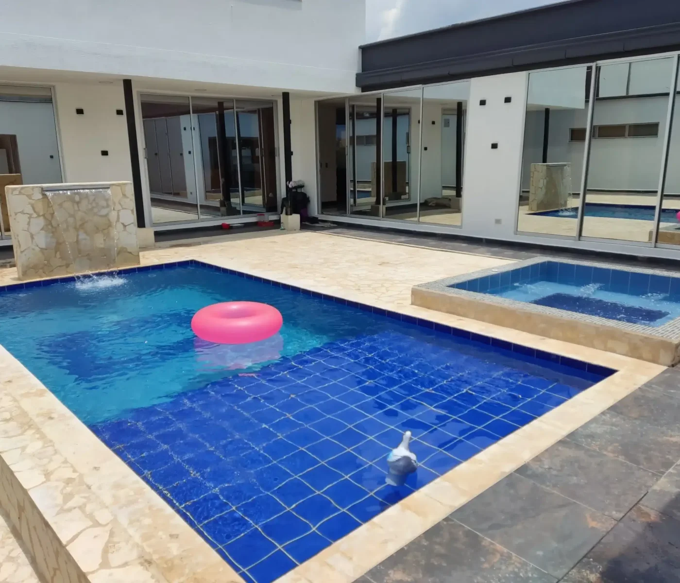 Piscina moderna creada por Piscinas Bluespace en Belén, Medellín, con azulejos azules, cascada decorativa y jacuzzi integrado. Diseño residencial que combina lujo y comodidad en un espacio exclusivo y contemporáneo